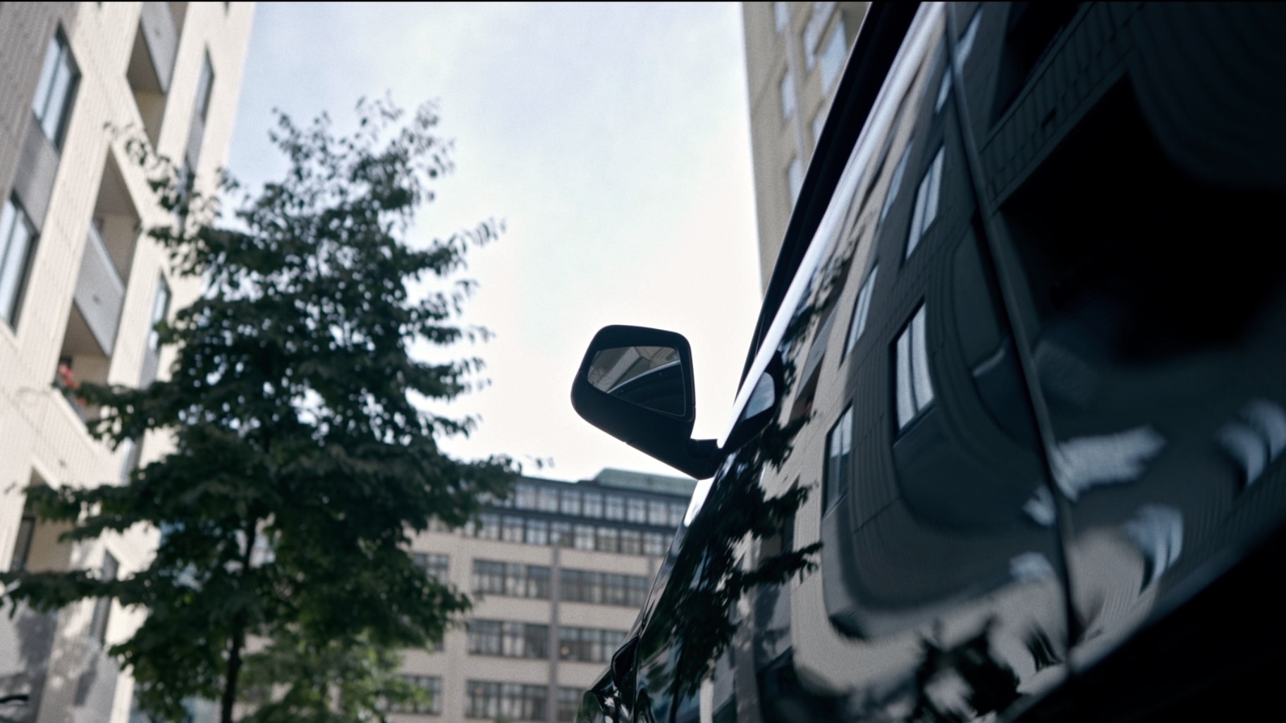 En svart bil fotat nedifrån med höghus som sträcker sig i bakgrunden.